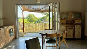 Ein geräumiges Zimmer mit großem offenen Bereich, einem Esstisch mit Stühlen, einer Holzkabine und Blick auf einen Weinberg durch eine offene Tür.