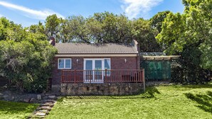 A brick house with a balcony, surrounded by a well-maintained lawn and trees. - Room in Guest Room - Garden Cottage, Houtbay, Cape Town, South Africa (Cape Town)