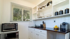 A kitchen with a built-in toaster oven, a microwave, and a coffee maker on the counter. There are cabinets with dishes and a window with blinds. - Room in Guest Room - Garden Cottage, Houtbay, Cape Town, South Africa (Cape Town)