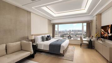 A modern hotel room with a large bed, a sofa, a desk with a chair, and a TV.