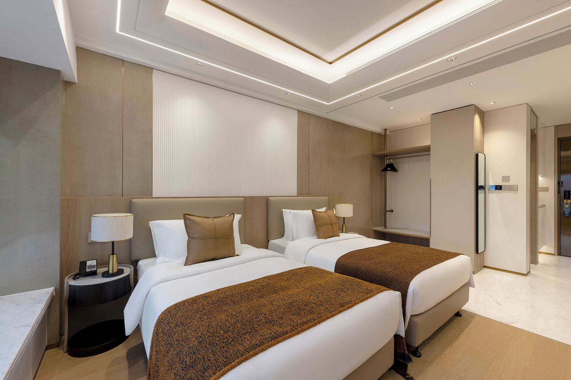 A hotel room with two beds, a bedside table with a lamp, a wardrobe, and a mirror.