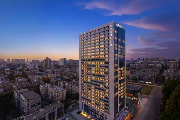 Un edificio alto y moderno con el nombre "ASCOTT" en la fachada, rodeado por una zona urbana densa y varios otros edificios.