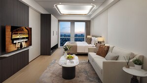 Ett modernt hotellrum med ett piano, en stor säng, en soffa, ett soffbord och utsikt över staden.