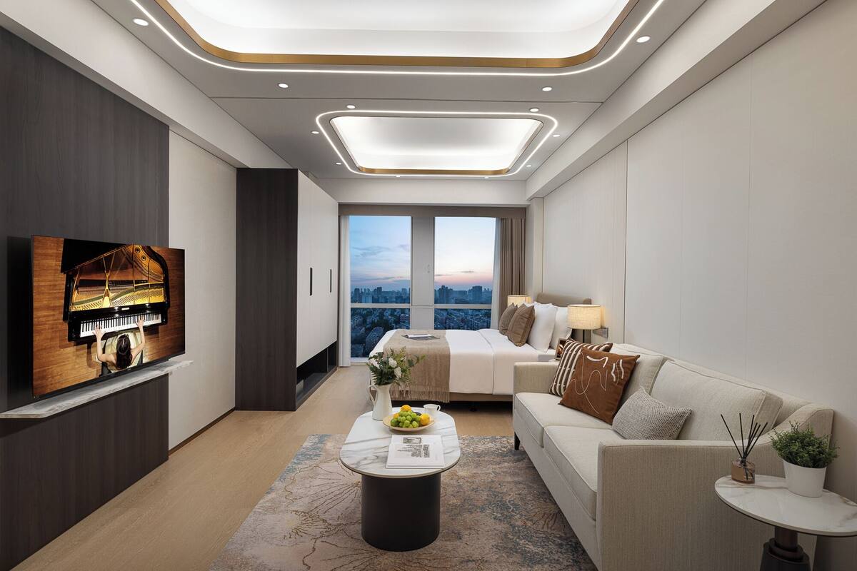 Een moderne hotelkamer met een piano, een groot bed, een bank, een salontafel en uitzicht op de stad.
