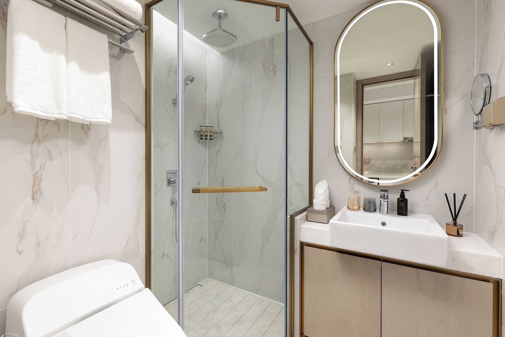 A modern bathroom with a glass-enclosed shower, a white sink with a gold frame, and a large mirror with a gold frame.