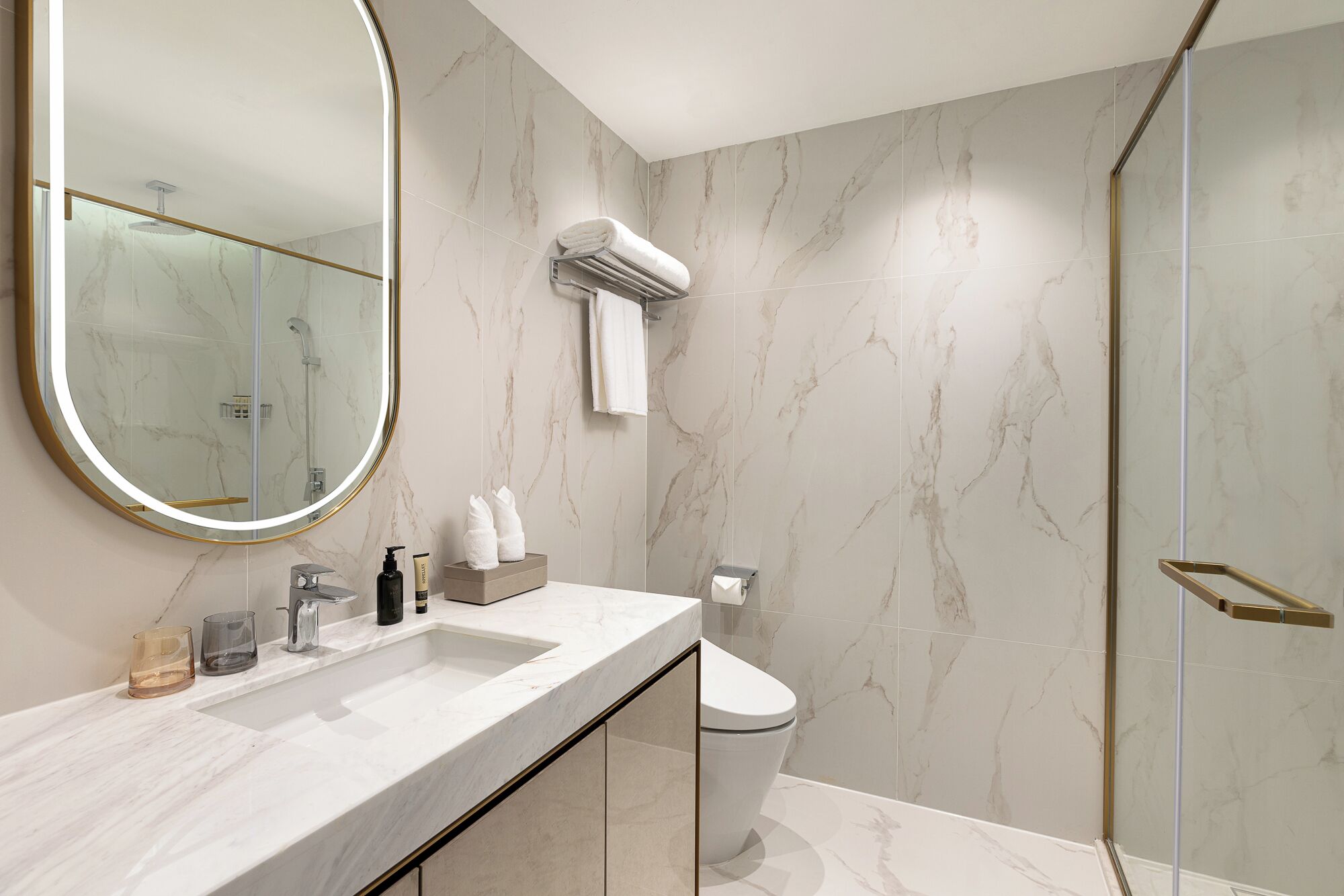 A modern bathroom with a marble vanity, a large mirror, a glass shower enclosure, and a toilet.