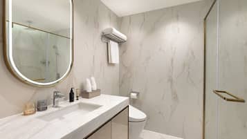 A modern bathroom with a marble vanity, a large mirror, a glass shower enclosure, and a toilet.