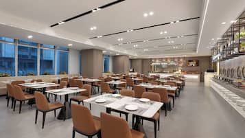A spacious restaurant with multiple dining tables and chairs, a bar area, and large windows offering views of the cityscape.