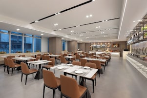 Un restaurante espacioso con varias mesas y sillas, una zona de bar y grandes ventanales con vistas a la ciudad.