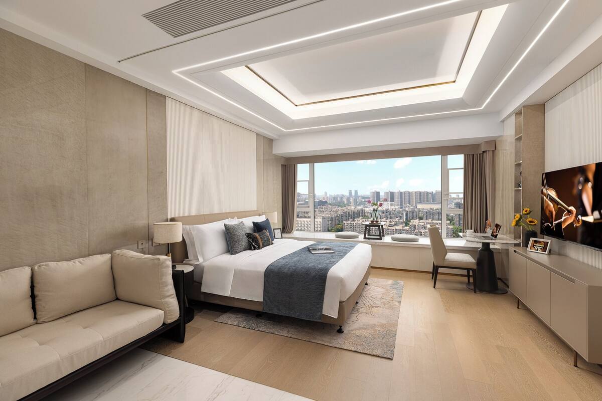 Een moderne hotelkamer met een groot bed, een bank, een bureau met stoel, en een televisie.