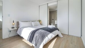 Ein modernes Schlafzimmer mit Bett, Nachttisch, Lampe und einer Schiebetür zum Kleiderschrank.