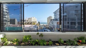 Blick aus einem Fenster mit einem Balkon, der auf eine belebte Straße mit Gebäuden und einem klaren Himmel zeigt.