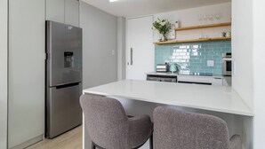 Eine moderne Küche mit einem Edelstahlkühlschrank, weißen Arbeitsplatten und einer gefliesten Spritzschutzwand.