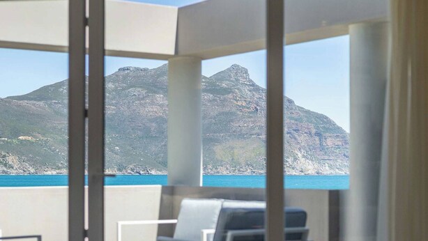 Un balcon avec vue sur la montagne et la mer. On y trouve des chaises et une table.