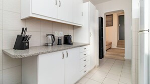 A modern kitchen with white cabinets, a granite countertop, and a coffee maker. There is a staircase leading to a dark room. - Charming Garden Cottage, Campsbay, Cape Town (Cape Town)