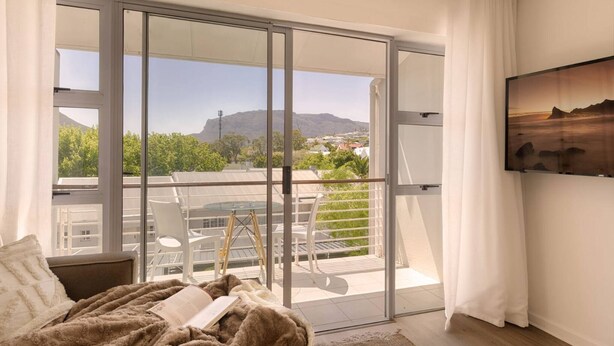 A bedroom with a large sliding glass door leading to a balcony with a view of a mountain and greenery.