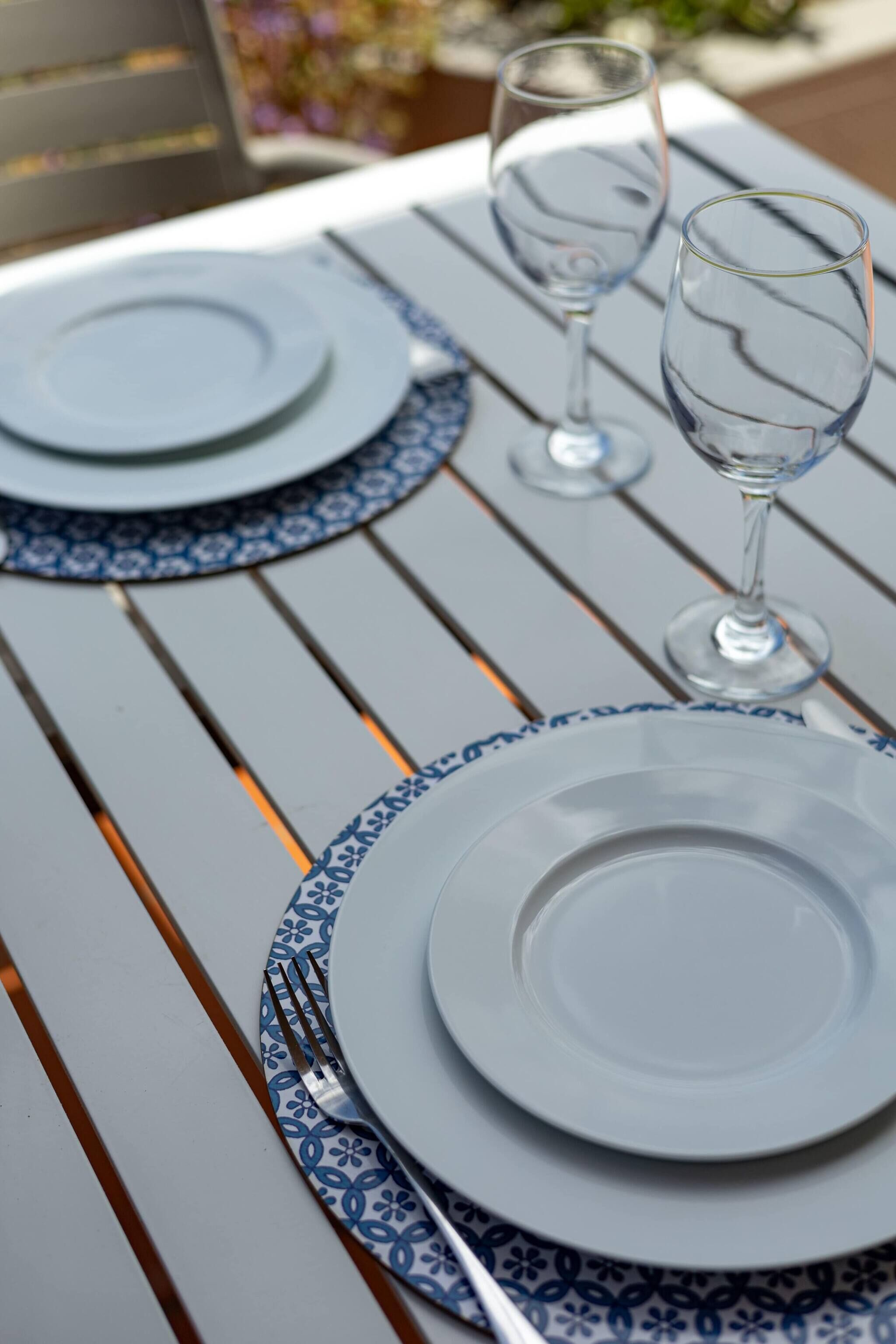 Una tavola imbandita con piatti, posate e bicchieri da vino, disposta su un tavolo di legno decorato con un motivo blu e bianco.