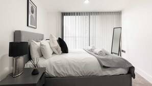 Een moderne slaapkamer met een bed, nachtkastje, lamp en een grote spiegel.