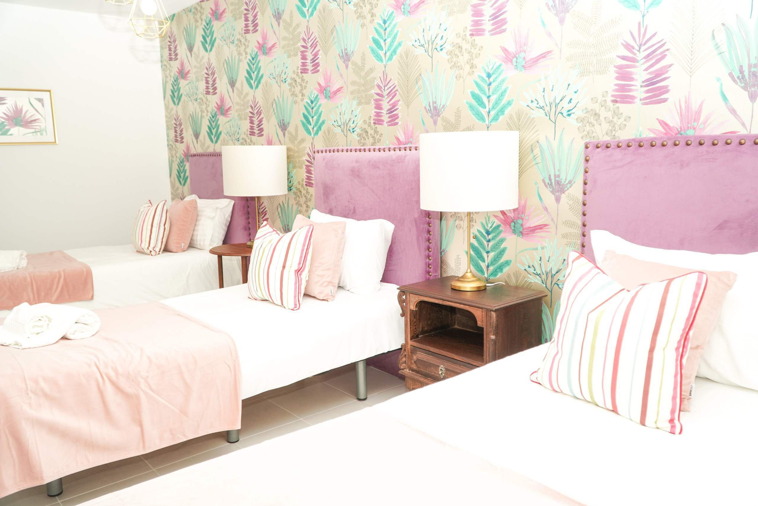 Ein Hotelzimmer mit zwei Betten, einem Nachttisch mit Lampe und einer Wand mit Blumenmuster.