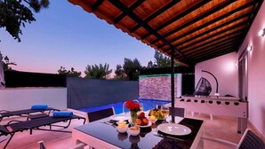 Un espace extérieur aménagé pour les repas, avec une table pour deux, une piscine et un coin salon abrité.