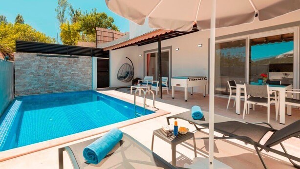 Une piscine extérieure avec des chaises longues et une table, un ventilateur, ainsi qu’un coin repas avec une table et des chaises.