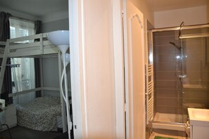 A bunk bed room with a bedside table and lamp, a bathroom with a glass shower enclosure, and a towel rack. - The Perfect Spot at Place de la Bastille - Bail Mobilité (Paris)
