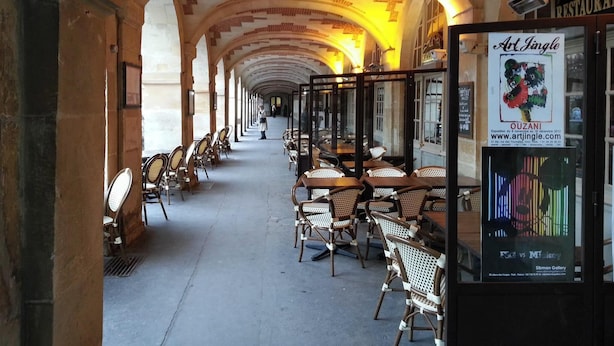 A corridor with arches and tables and chairs, leading to a restaurant. - The Perfect Spot on Place de la Bastille - Bail Mobilité (Paris)