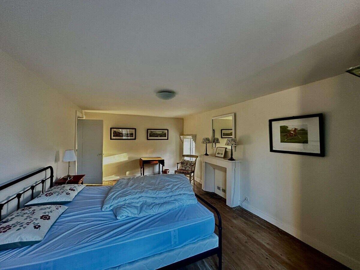 Un dormitorio con cama, una silla, un escritorio, chimenea y cuadros en la pared.