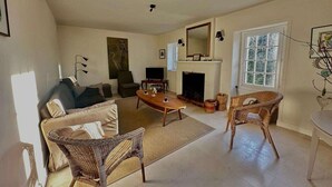 A spacious living room with a sofa, two wicker chairs, a coffee table, a fireplace, and a television. - The gardener's house (Tracy-sur-Mer)