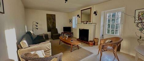 A spacious living room with a sofa, two wicker chairs, a coffee table, a fireplace, and a television.