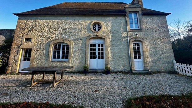 A stone building with a central door, two windows on either side, and a small table in front. - The gardener's house (Tracy-sur-Mer)