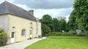 A stone building with a gravel driveway leading to a grassy area. - The gardener's house (Tracy-sur-Mer)