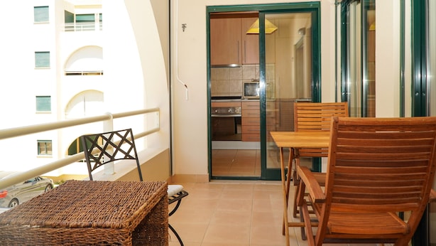 A balcony with a wicker table and chairs, a view of a building, and a sliding glass door leading to a kitchen with a microwave and cabinets. - Sacada Apartment - Great Balcony (Guia)