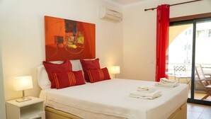 A hotel room with a large bed, red and white pillows, a nightstand with a lamp, and a view of the outside balcony. - Sacada Apartment - Great Balcony (Guia)