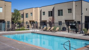 A swimming pool with lounge chairs and a barbecue grill, surrounded by a fence and modern buildings.