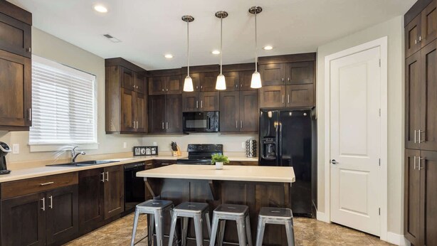 A modern kitchen with dark wood cabinets, a central island with stools, a stainless steel refrigerator, and a microwave.