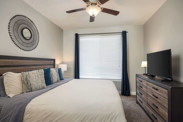 A bedroom with a bed, a ceiling fan, a TV, and a dresser. - Downtown Moab Basecamp Pool & Hot Tub - Entrada (Moab)