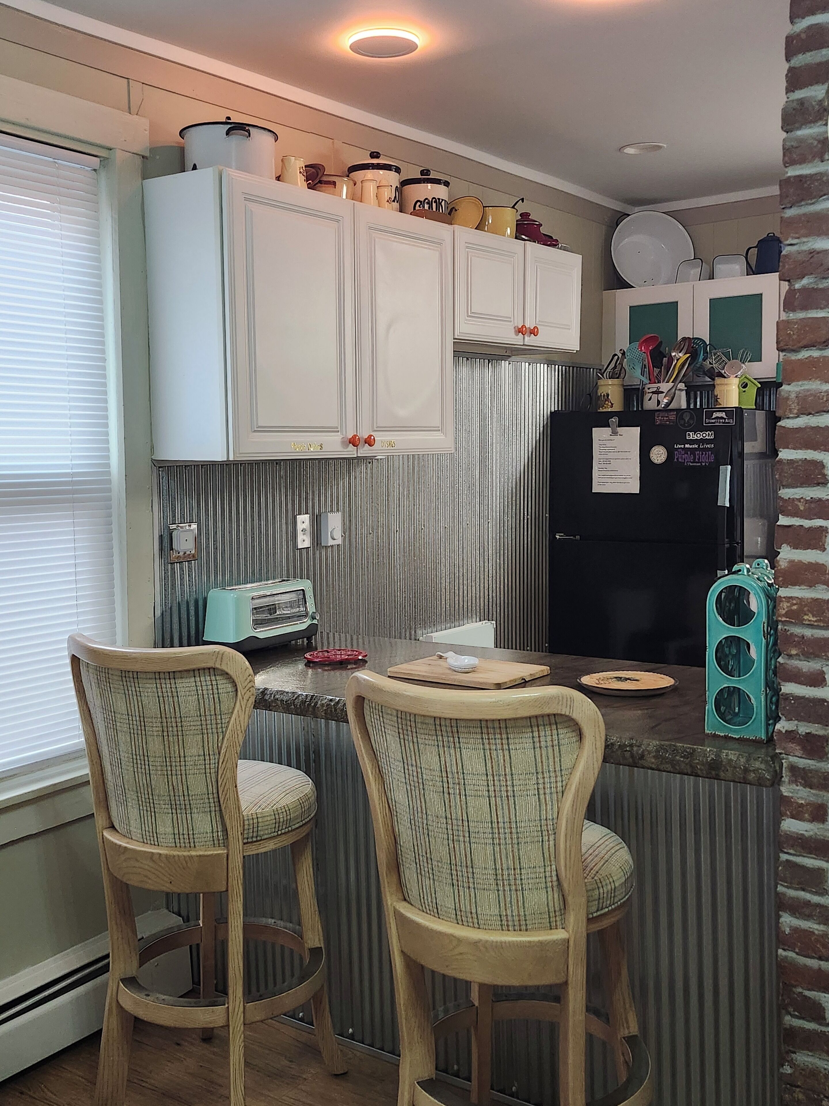 A kitchen with two bar stools, a refrigerator, and various kitchen items on the counter.