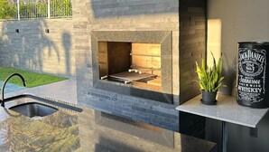 Una cocina exterior moderna con una parrilla empotrada, un lavamanos y una planta en maceta.