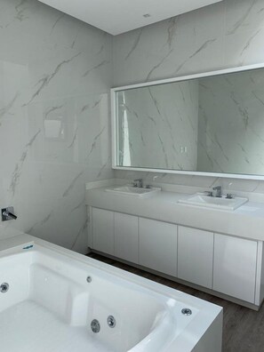 A modern bathroom with a marble backsplash, a large mirror, two sinks, and a freestanding bathtub.