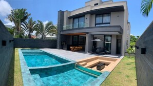 Una casa moderna de dos pisos con piscina, mobiliario exterior y un jardín bien cuidado.