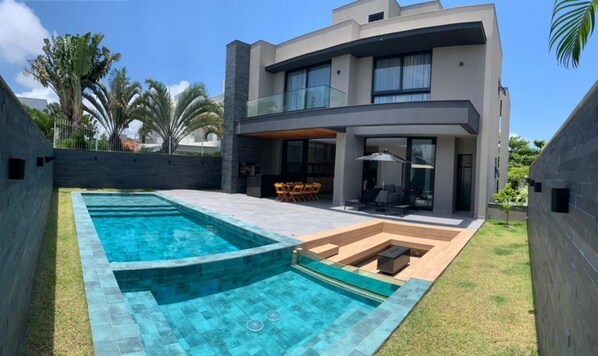 Una casa moderna de dos pisos con piscina, mobiliario exterior y un jardín bien cuidado.