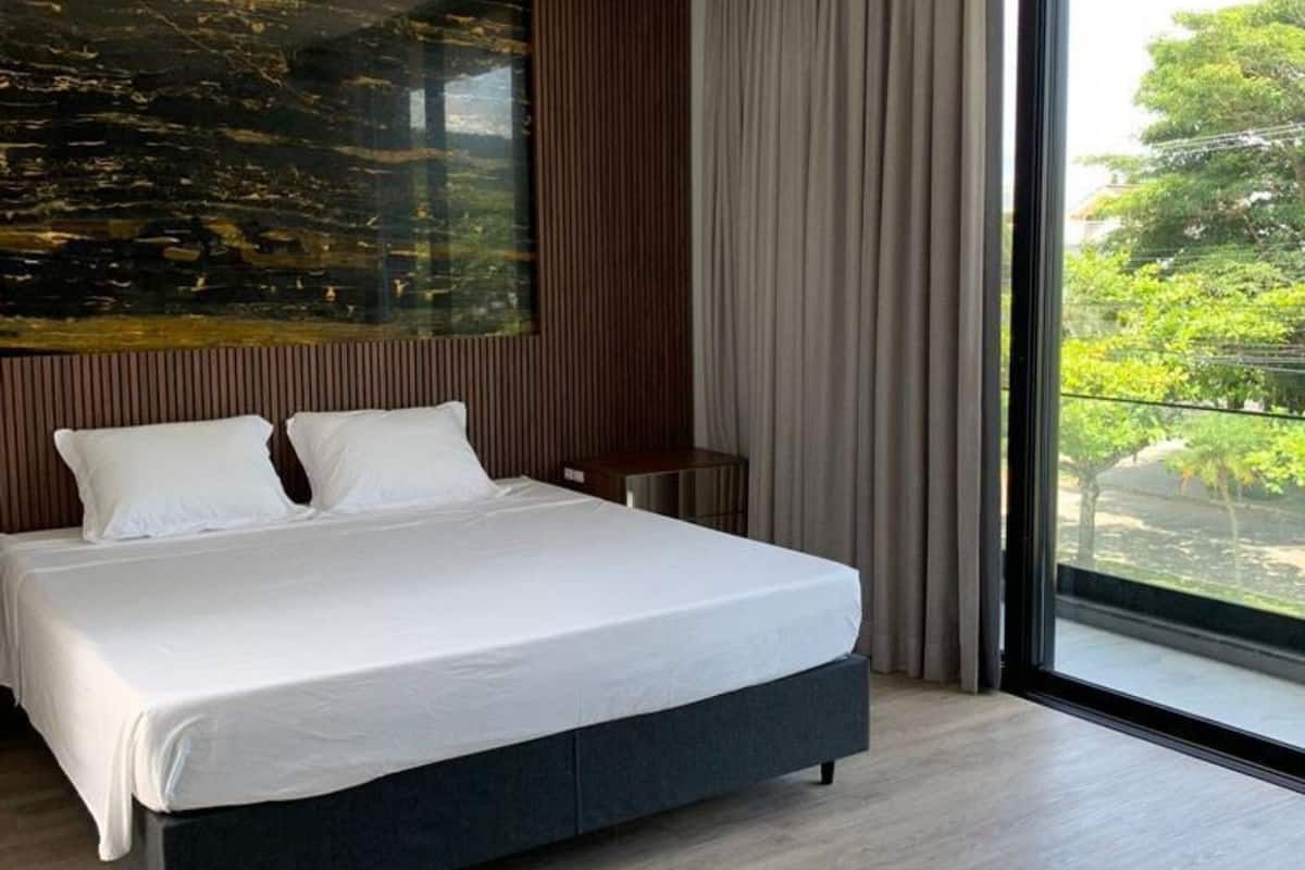Un dormitorio moderno con una cama grande, un panel decorativo de madera y un ventanal con vistas a zonas verdes.