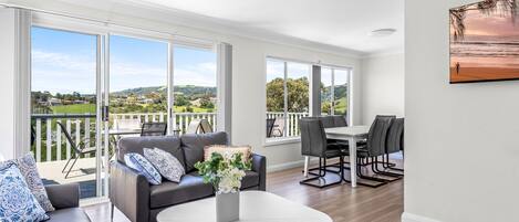 Ein geräumiges Wohnzimmer mit Balkon, großen Fenstern und einem Essbereich.