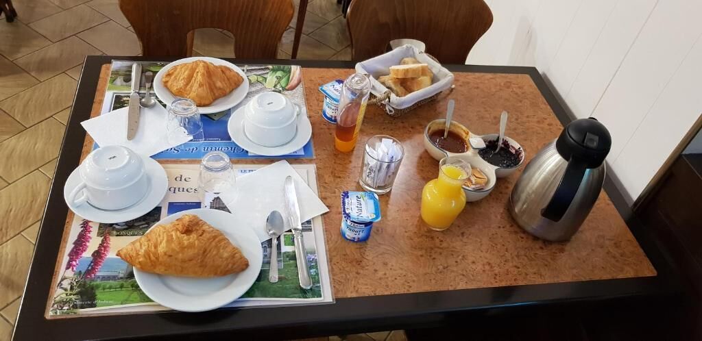 Aamiaispöydällä on croissantteja, kuppi, lasi appelsiinimehua, termospullo ja sanomalehti.