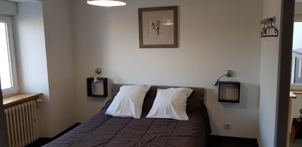 Ein Schlafzimmer mit einem Bett, zwei Nachttischen, einem Heizkörper, einem Fenster und einem gerahmten Bild an der Wand.