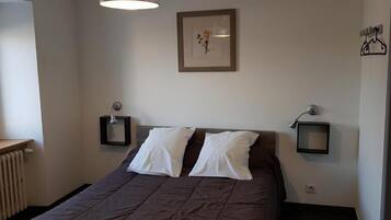 Ein Schlafzimmer mit einem Bett, zwei Nachttischen, einem Heizkörper, einem Fenster und einem gerahmten Bild an der Wand.