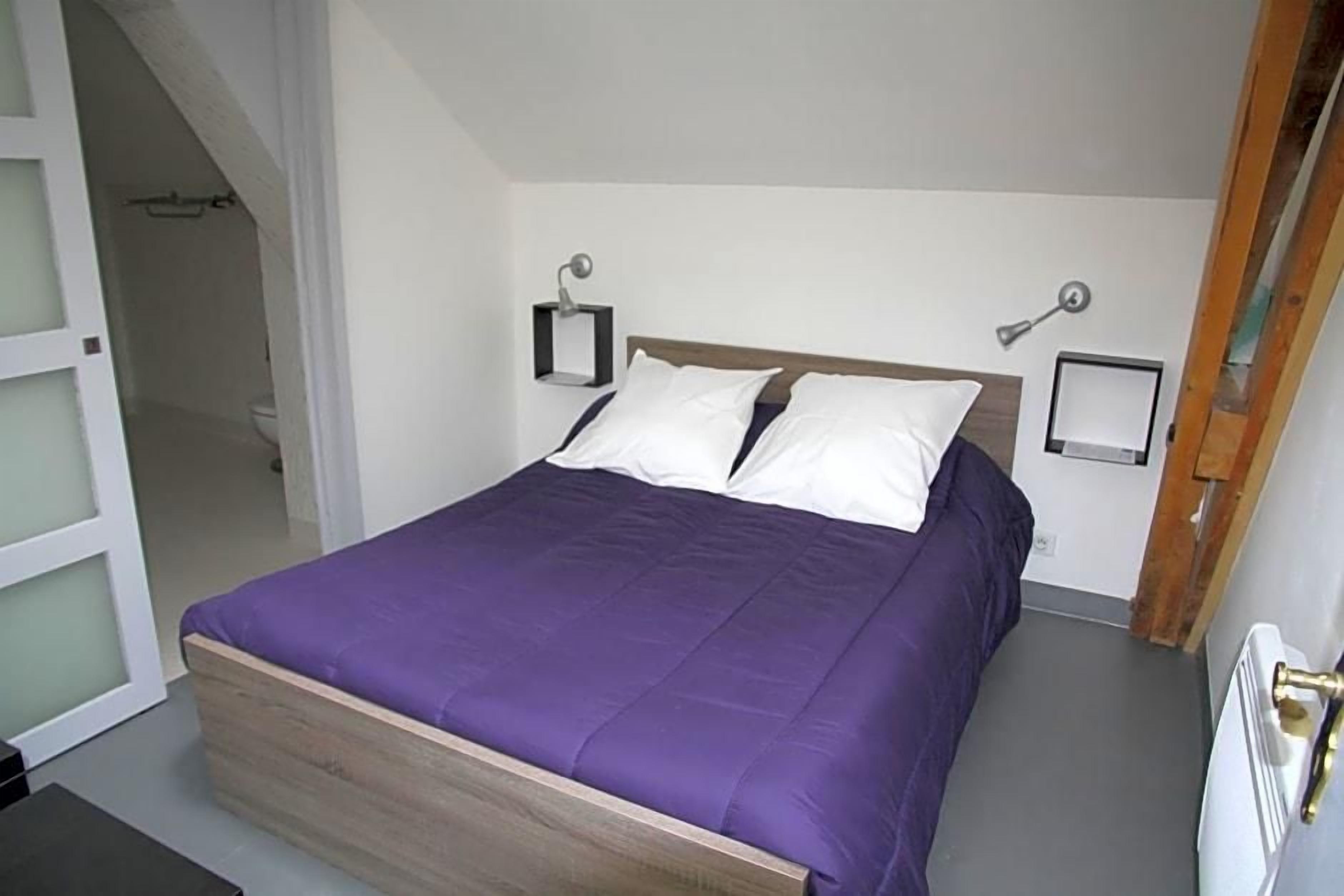 A bedroom with a bed, a nightstand, and a wall-mounted lamp.
