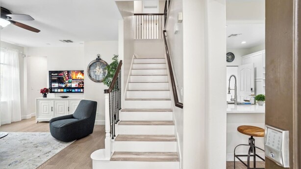 Una sala de estar moderna con una escalera, un televisor de pantalla plana, un sillón cómodo y una zona de cocina.