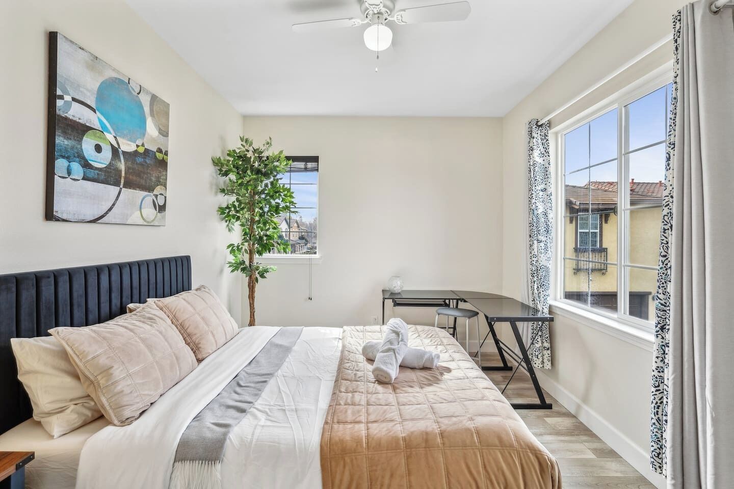 A bedroom with a bed, a desk, a potted plant, and a window with curtains.